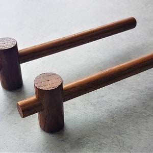 Könnte beinhalten: Zwei Holzknaufgriffe mit T-förmigem Design. Die Griffe sind aus dunkelbraunem Holz und haben eine glatte Oberfläche.