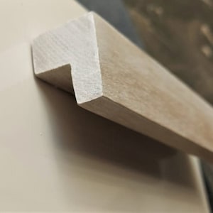 May include: A light brown wooden drawer pull with a simple, rectangular design. The pull has a slightly distressed finish, giving it a rustic look.