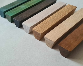 Op de afbeelding: Zeven houten ladegrepen in verschillende tinten groen, bruin, grijs en naturel hout. De grepen zijn allemaal driehoekig van vorm en hebben een gladde, gepolijste afwerking.