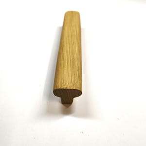 May include: A light brown wooden cabinet handle with a smooth, elongated top surface and a T-shaped profile. The natural wood grain is visible across the length of the handle, which features rounded edges and a solid, sturdy construction.