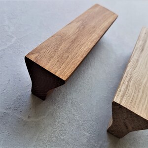 Puede incluir: Dos tiradores de armario de madera con forma triangular. El tirador de la izquierda es de madera marrón oscura, mientras que el tirador de la derecha es de madera marrón clara.