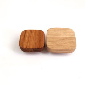 以下が含まれることがあります： 2つの正方形の木製の壁掛けフック。1つは濃い茶色、もう1つは明るい自然な木の色です。