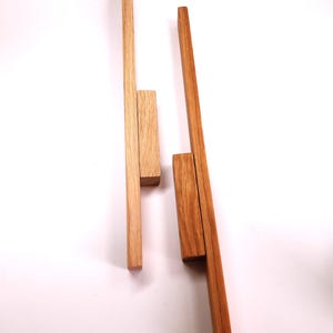 May include: Two wooden dowels, one light brown and one dark brown, are arranged vertically on a white background. The dowels are both about 12 inches long and 1 inch wide. The light brown dowel has a smaller piece of wood attached to it near the top. The dark brown dowel has a smaller piece of wood attached to it near the bottom.