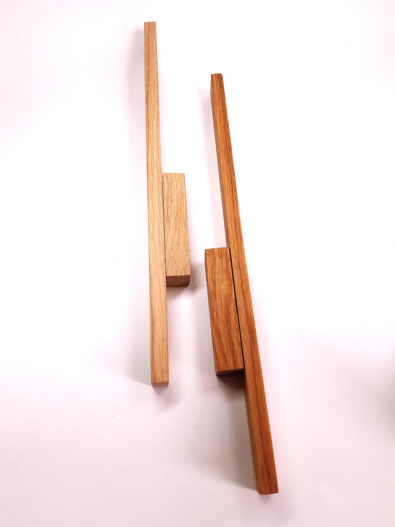 May include: Two wooden dowels, one light brown and one dark brown, are arranged vertically on a white background. The dowels are both about 12 inches long and 1 inch wide. The light brown dowel has a smaller piece of wood attached to it near the top. The dark brown dowel has a smaller piece of wood attached to it near the bottom.
