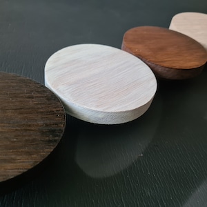 Peut inclure: Cinq sous-verres ronds en bois dans différentes nuances de brun, blanc et beige. Les sous-verres sont disposés en rangée du plus foncé au plus clair.