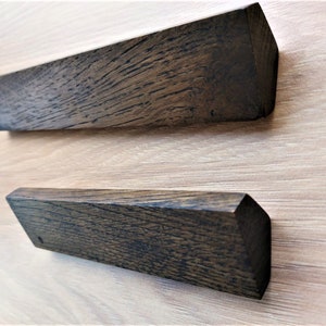May include: Two dark brown wooden drawer pulls with a slightly rounded rectangular shape. The pulls have a natural wood grain and a dark stain.