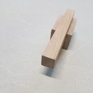 Puede incluir: Un bloque de madera con un bloque de madera más pequeño unido a la parte superior. El bloque más grande está colocado en un ángulo de 45 grados.