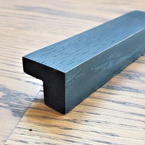 May include: Black wooden T-shaped cabinet pull with a smooth, slightly textured finish.