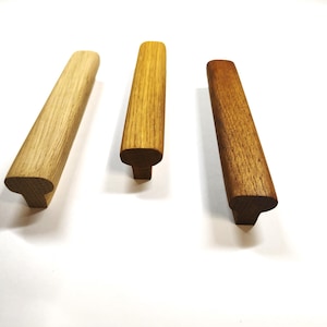 May include: Three wooden cabinet pulls arranged in a row, each featuring a distinct wood grain pattern and color variation. The handles have a T-shaped profile with a rounded top surface and a rectangular base, showcasing light, medium, and dark wood tones.