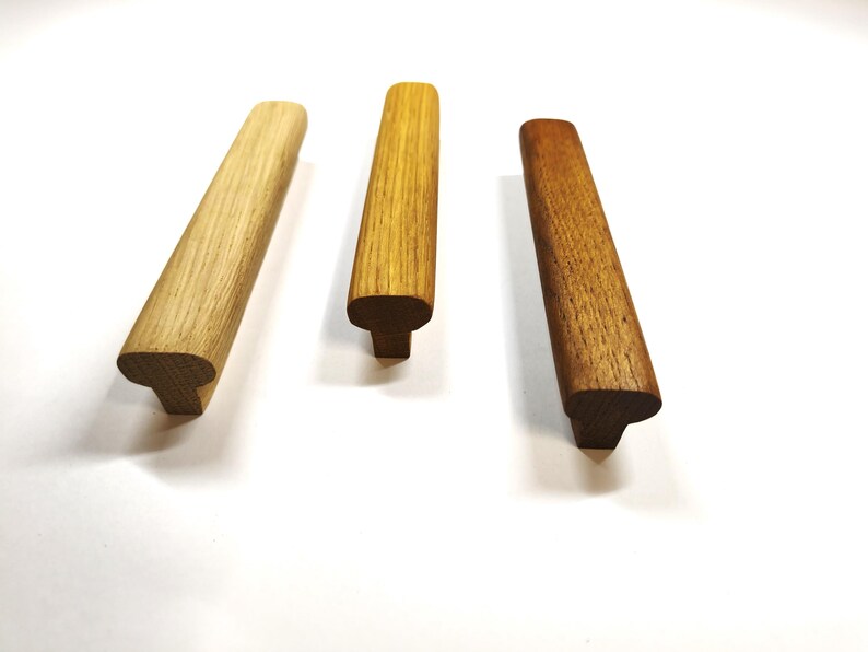 May include: Three wooden cabinet pulls arranged in a row, each featuring a distinct wood grain pattern and color variation. The handles have a T-shaped profile with a rounded top surface and a rectangular base, showcasing light, medium, and dark wood tones.