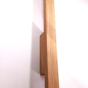 May include: A wooden wall-mounted shelf with a natural wood finish. The shelf is made of solid wood and has a simple, modern design.