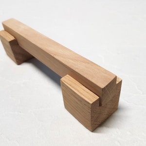 Puede incluir: Una manija de armario de madera con forma rectangular y acabado en madera natural.
