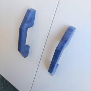 May include: Two blue cabinet door handles with a geometric design. The handles are mounted on a white cabinet door.