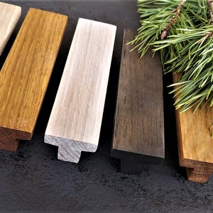 May include: Six wooden cabinet pulls in various shades of brown, white, and gray. The pulls have a T-shaped design and are arranged in a row on a dark surface.