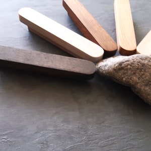 Peut inclure: Un ensemble de six poignées de tiroir en bois dans différentes nuances de brun, blanc et bois naturel. Les poignées sont disposées en éventail sur une surface texturée grise, avec un petit rocher gris au centre.