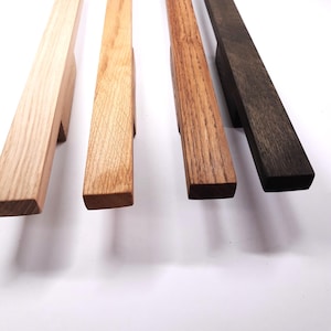 Op de afbeelding: Vier houten kastgrepen in verschillende houttinten, van licht tot donker. De grepen zijn rechthoekig en hebben een gladde, gepolijste afwerking.