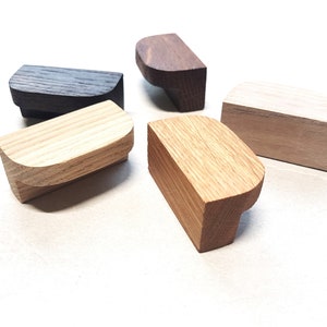 May include: Five wooden cabinet knobs in different shades of brown. The knobs are all half-round in shape and have a smooth, polished finish.