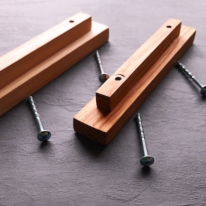 Puede incluir: Dos soportes de estantería de madera con agujeros preperforados y tornillos. Los soportes son de madera marrón claro y están listos para ser instalados.