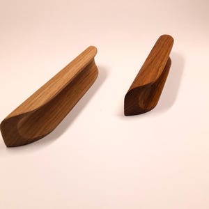 May include: Two wooden cabinet pulls with a curved design. The pulls are made of light brown wood and have a smooth finish.