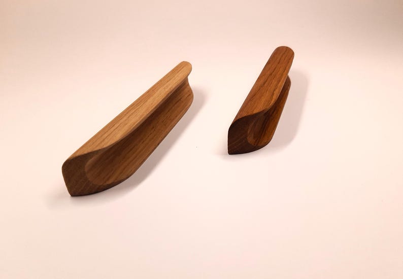 May include: Two wooden cabinet pulls with a curved design. The pulls are made of light brown wood and have a smooth finish.