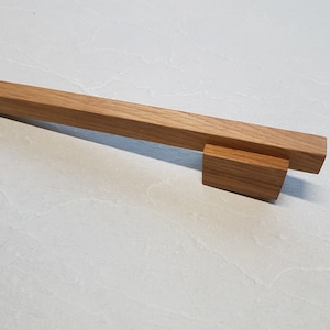 May include: A wooden cabinet door handle with a rectangular shape and a natural wood finish.