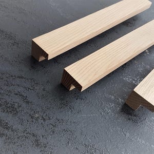 May include: Three wooden drawer pulls in various sizes. The pulls are made of light brown wood and have a simple, rectangular shape with a slight curve at the top.