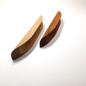 May include: Two wooden cabinet pulls, one light brown and one dark brown, with a curved shape and a cutout in the center.