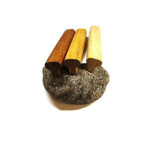 May include: Three wooden cabinet pulls with a T-shaped profile, arranged in a row. The pulls feature varying wood tones, ranging from a dark brown to a medium golden brown and a light tan, each displaying a natural wood grain texture.