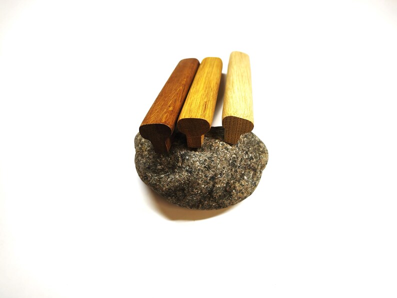 May include: Three wooden cabinet pulls with a T-shaped profile, arranged in a row. The pulls feature varying wood tones, ranging from a dark brown to a medium golden brown and a light tan, each displaying a natural wood grain texture.