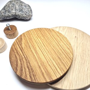 May include: Two circular wooden discs with visible grain patterns, one darker and one lighter in colour, accompanied by two small cylindrical wooden knobs with metal screws inserted into the centres and a single grey speckled stone.