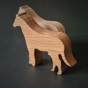 Puede incluir: Dos figuritas de animales de madera, una detrás de la otra, ambas talladas en forma de caballo. El caballo de delante está mirando hacia el lado derecho de la imagen, mientras que el caballo de atrás está mirando hacia el lado izquierdo de la imagen. Ambos caballos están hechos de madera marrón claro.