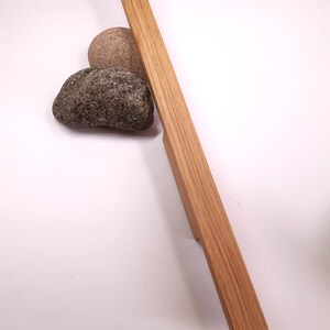 May include: A long, rectangular, wooden cabinet pull with a natural wood finish. The pull is made of solid oak and has a smooth, slightly textured surface.