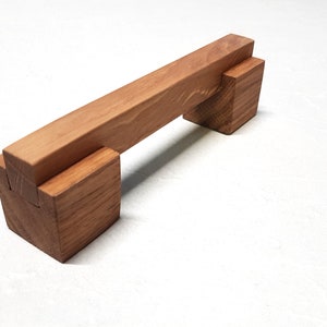 May include: A wooden cabinet door handle with a rectangular shape and a natural wood finish.