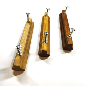 May include: Three rectangular wooden drawer pulls with a smooth finish, each featuring two silver metal screws protruding from the front. The pulls vary in wood grain color, ranging from light tan to a deeper, richer brown tone.