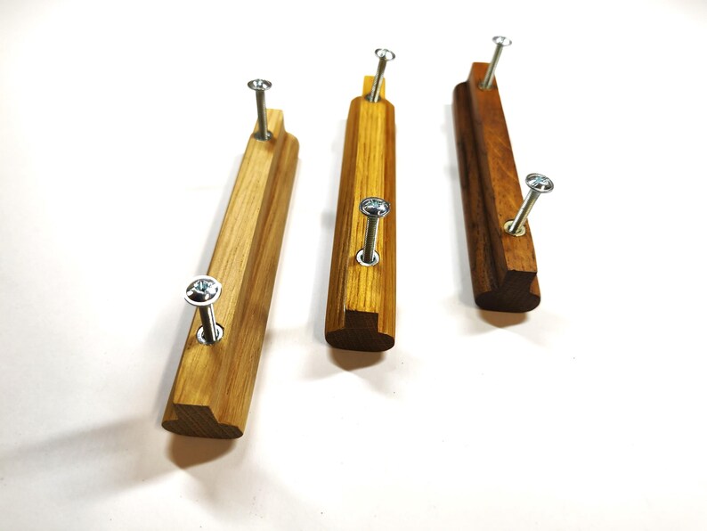 May include: Three rectangular wooden drawer pulls with a smooth finish, each featuring two silver metal screws protruding from the front. The pulls vary in wood grain color, ranging from light tan to a deeper, richer brown tone.