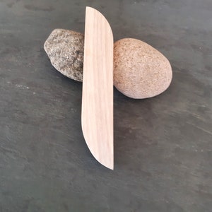 Op de afbeelding: Een lichtbruine houten carving in de vorm van een lang, dun, gebogen blad. De carving rust op twee ronde, grijze en bruine stenen.