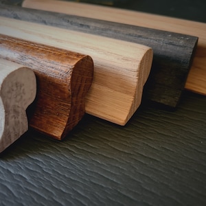 Op de afbeelding: Vijf houten lijstdelen in verschillende tinten bruin, wit en zwart. De lijstdelen hebben allemaal dezelfde vorm en grootte, met een afgeronde rand en een platte onderkant.