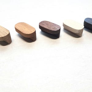 May include: Five wooden drawer pulls in different wood tones. The pulls are oval shaped and have a smooth finish.