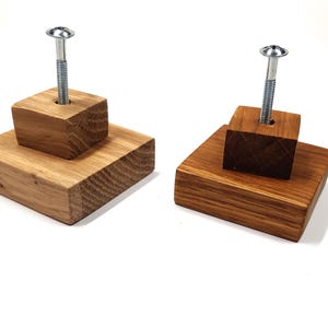 May include: Two wooden wall hooks with a screw in the centre. The hooks are made of natural wood with a light brown finish. The hooks are stacked on top of each other.