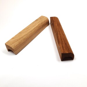 May include: Two wooden cabinet pulls, one light brown and one dark brown. Both pulls have a curved shape and a rounded edge.