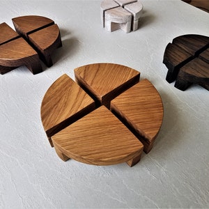 Può includere: Quattro sottobicchieri in legno di diversi colori, ognuno composto da quattro pezzi a quarto di cerchio che si incastrano per formare un cerchio. I sottobicchieri sono in legno chiaro, legno scuro e legno bianco.