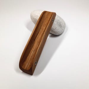 May include: A wooden, brown, rectangular tray with rounded edges and two silver screws. The tray is sitting on a white, round, smooth stone.