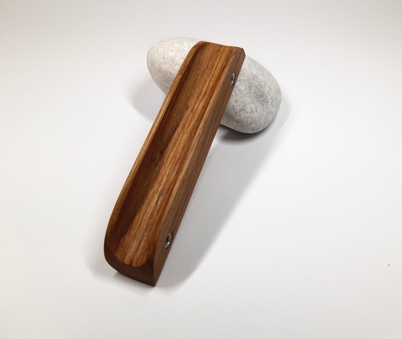 May include: A wooden, brown, rectangular tray with rounded edges and two silver screws. The tray is sitting on a white, round, smooth stone.