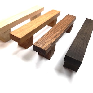 May include: Four wooden drawer pulls in different shades of brown. The pulls are rectangular with rounded edges and a square base.