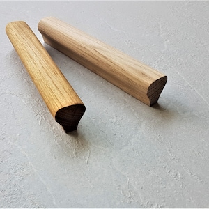 Peut inclure: Deux poignées de tiroir en bois avec des bords arrondis. Les poignées sont en bois brun clair et ont une finition lisse.