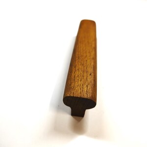 May include: A medium brown wooden cabinet pull with a smooth, elongated, and slightly curved top surface. The handle features a visible natural wood grain pattern and a T-shaped profile, showcasing a sturdy construction and a warm, earthy tone.