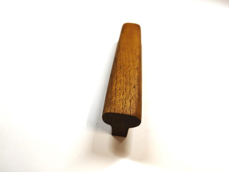 May include: A medium brown wooden cabinet pull with a smooth, elongated, and slightly curved top surface. The handle features a visible natural wood grain pattern and a T-shaped profile, showcasing a sturdy construction and a warm, earthy tone.