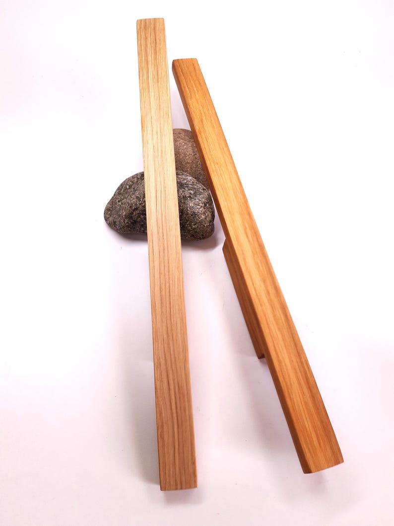 May include: Two wooden cabinet pulls with a natural wood finish. The pulls are rectangular in shape and have rounded edges.
