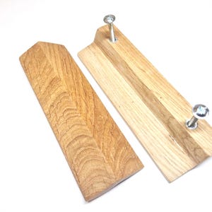 Könnte beinhalten: Zwei rechteckige, hellbraune Holzwandhaken mit natürlicher Holzmaserung. Ein Haken ist von vorne zu sehen, der andere von hinten, wobei zwei silberne Metallschrauben aus der Holzoberfläche herausragen.