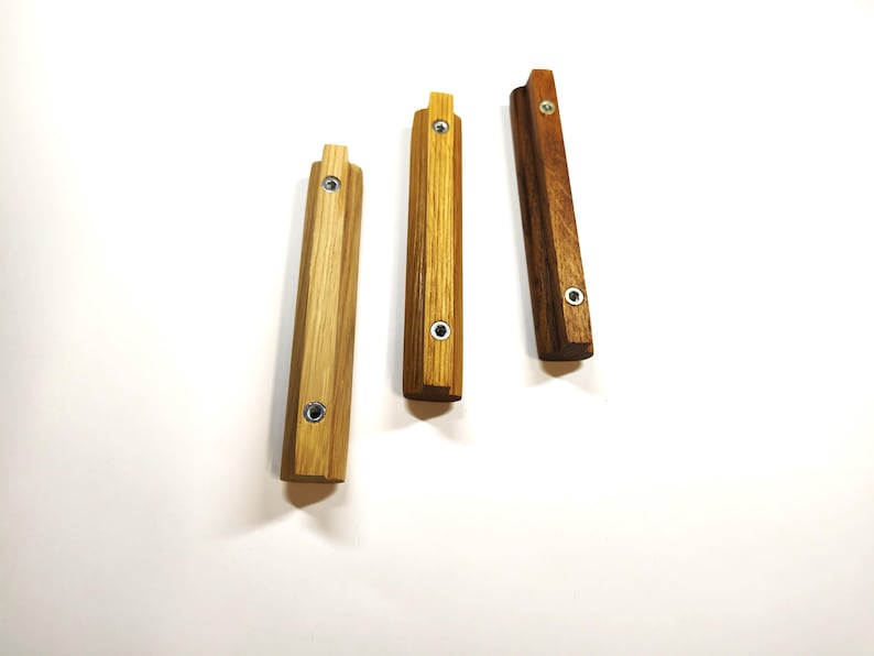 May include: Three rectangular wooden cabinet pulls arranged vertically. Each pull features a distinct wood grain pattern, ranging from light to dark brown, and includes two circular metal screw holes for mounting purposes on furniture.